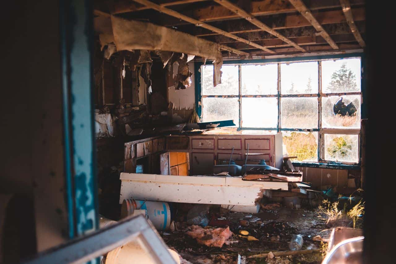 Interior of abandoned ruined building with broken window and damaged furniture with trash on floor in daylight in countryside inside